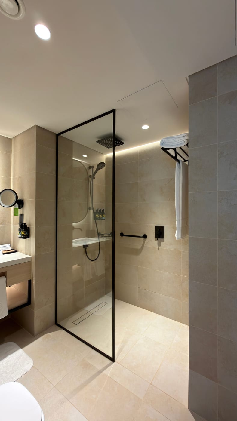 Vom Fliesenleger gebaute bodengleiche Walk-in-Dusche mit schwarz gerahmter Glasabtrennung und Haltegriff