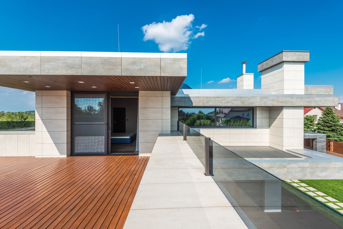 Vom Fliesenleger verlegte Terrassenfliesen neben einer Holzterrasse an einem modernen Einfamilienhaus